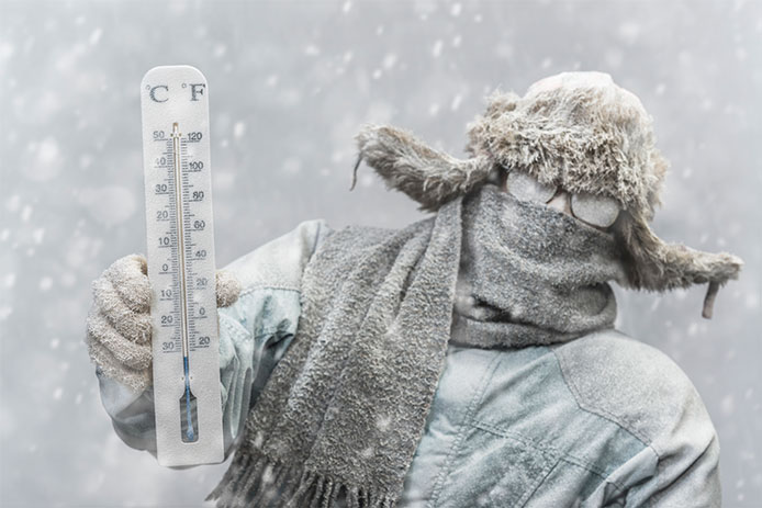 A frozen Caucasian male holding a mercury thermometer that reads -20 F (-32C) looking at the camera, while outside in a snow storm. He is all bundled up in a fur trapper's hat, scarf, parka, and gloves, His eye glasses and the rest of him is covered in snow and frost.