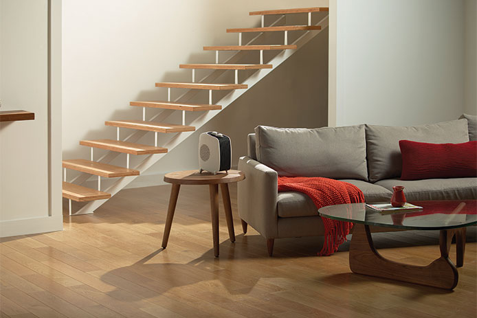 White heater sitting on wooden side table in a living room, with a gray couch and red blanket