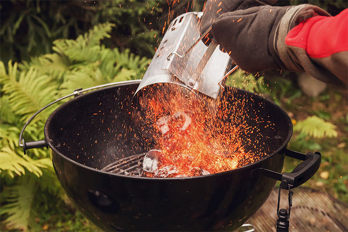 Preparation of barbeque grill with hinged lid using chimney starter for igniting charcoal or briquettes - stock photo