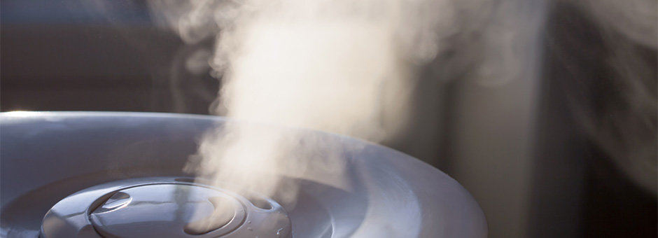 A puff of humidity leaves the top of a grey humidifier.